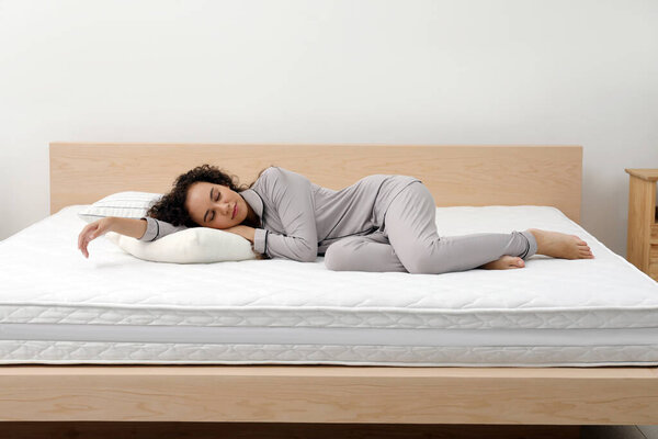Young African American woman sleeping on bed with comfortable mattress and pillow at home