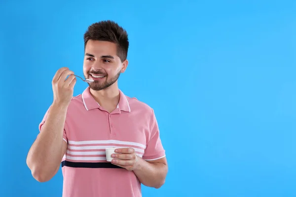 Happy young man eating tasty yogurt on light blue background. Space for text