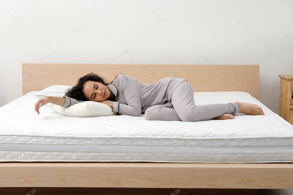 Young African American woman sleeping on bed with comfortable mattress and pillow at home