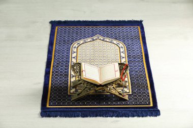 Rehal with open Quran and Misbaha on Muslim prayer rug indoors