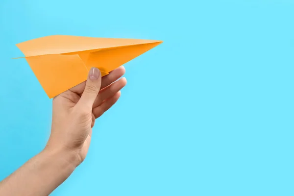 Woman holding orange paper plane on light blue background, closeup. Space for text