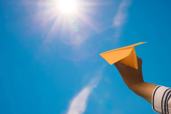 Woman holding orange paper plane against blue sky, closeup. Space for text