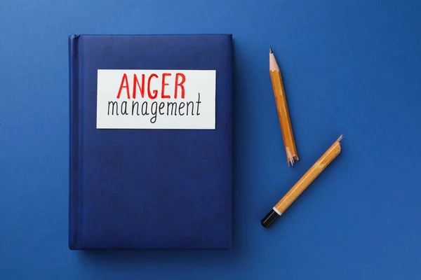 Notebook with words Anger Management and broken pencil on blue background, flat lay