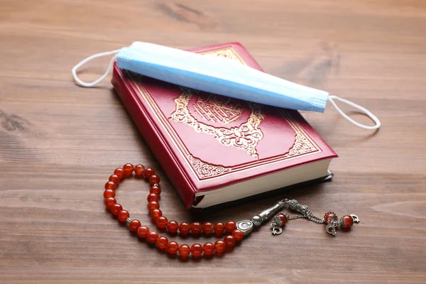 Muslim prayer beads, Quran and medical mask on wooden table