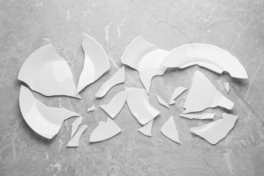 Two broken ceramic plates on light grey table, flat lay