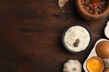 Creamy caper sauce in bowl and ingredients on wooden table, flat lay. Space for text