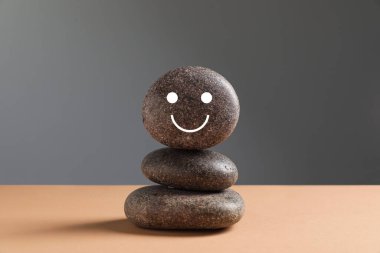 Gri arka planda bej masanın üzerine çizilmiş gülen yüzlü taşlar yığını. Zen kavramı