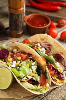 Kızarmış pastırmalı lezzetli tacolar ve ahşap masada limon, yakın plan.