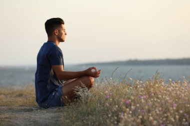 Güneşli bir günde nehrin kenarında meditasyon yapan bir adam.