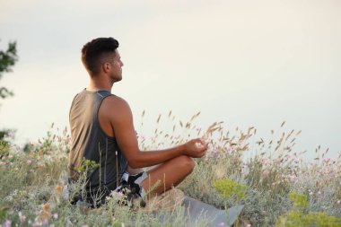 Nehir kenarındaki çayırda meditasyon yapan bir adam. Metin için boşluk