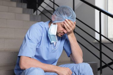 Hastanede merdivenlerde oturan bitkin doktor.