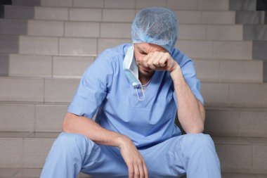 Hastanede merdivenlerde oturan bitkin doktor.