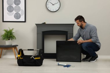 Man installing electric fireplace near wall in room