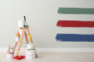 Decorator's kit of tools and paints near white wall with samples of different paints indoors