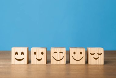 Cubes with different emoticons in row on wooden table against light blue background