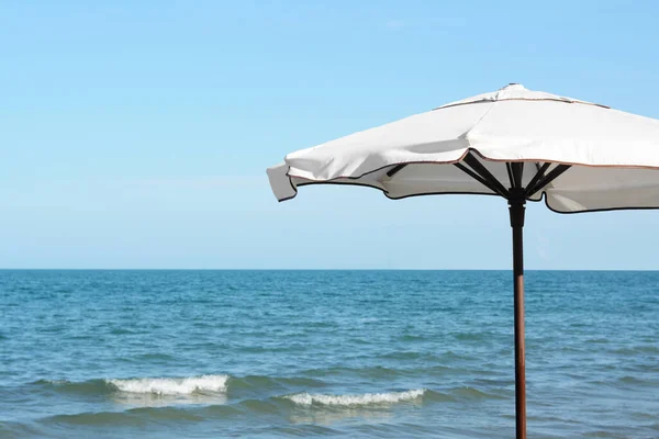 Beautiful white beach umbrella near sea on sunny day, space for text