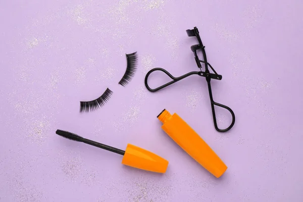 False eyelashes, curler and mascara on violet background, flat lay