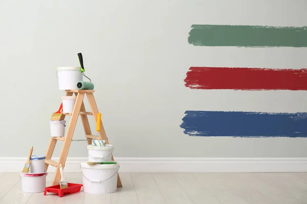 Decorator\'s kit of tools and paints near white wall with samples of different paints indoors