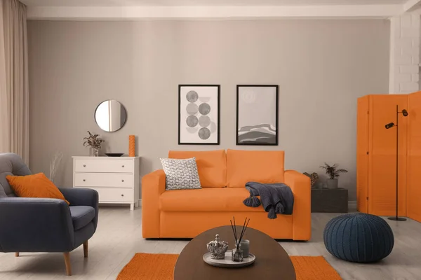 Stylish living room interior with orange sofa, armchair and beautiful pictures