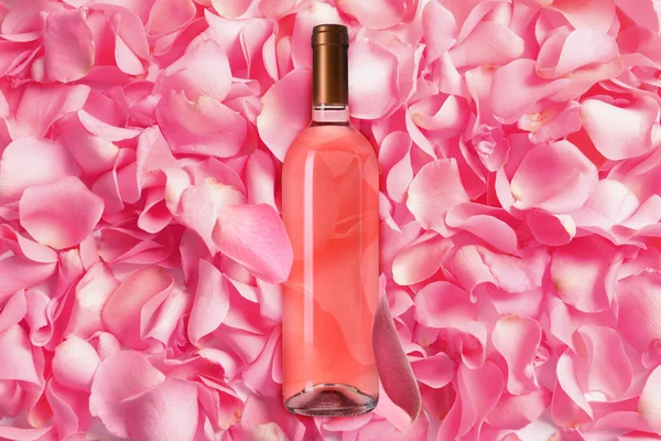 Bottle of delicious rose wine and pink petals, top view