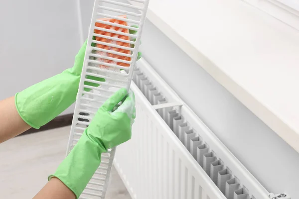 Woman washing radiator grill with sponge and detergent indoors, closeup. Space for text