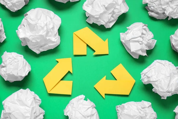 Recycling symbol and crumpled paper on green background, flat lay