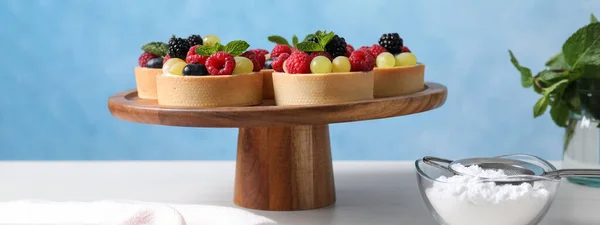 Delicious tartlets with berries on white table. Banner design