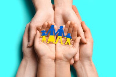 Parents and child holding paper family cutout in colors of Ukrainian flag at cyan table, top view