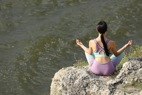 Young Woman Meditating Cliff River Back View Space Text — стоковое фото
