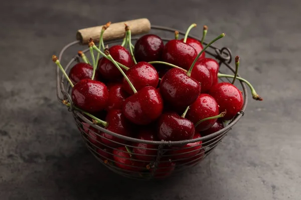 Metal basket with ripe sweet cherries on dark grey table, closeup