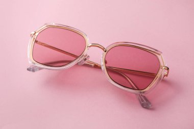 Pembe arka planda yeni moda güneş gözlükleri, yakın plan. Modaya uygun aksesuarlar.