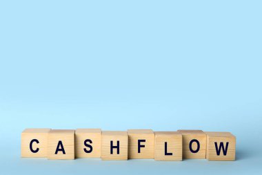 Wooden cubes with phrase Cash FLow on light blue background. Space for text