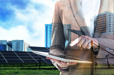 Double exposure of businesswoman with tablet and solar panels installed outdoors. Alternative energy source