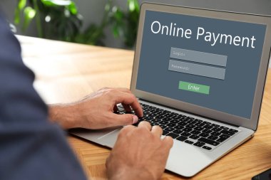 Man using laptop for online payment at wooden table, closeup