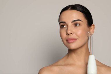 Gri arka planda yüksek frekanslı darsonval cihaz kullanan bir kadın. Metin için boşluk