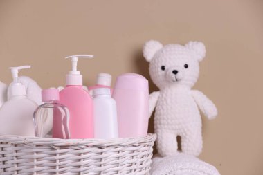Bebek kozmetik ürünleri ve bej arka planda örülmüş oyuncak ayıyla dolu bir sepet.