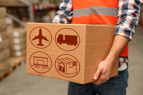 Worker with cardboard box with shipping icons in warehouse, closeup. Wholesaling