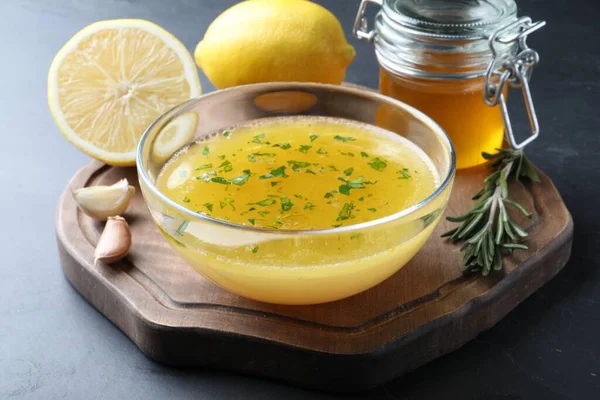 Bowl with lemon sauce and ingredients on dark table. Delicious salad dressing