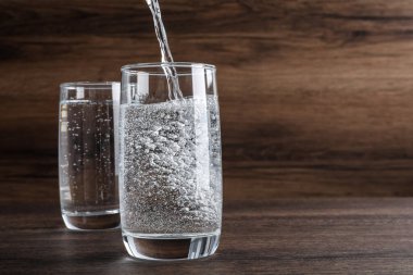 Pouring soda water into glass on wooden table. Space for text