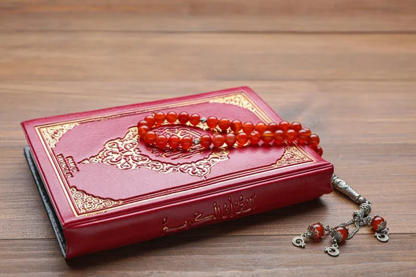 Muslim prayer beads and Quran on wooden table, closeup
