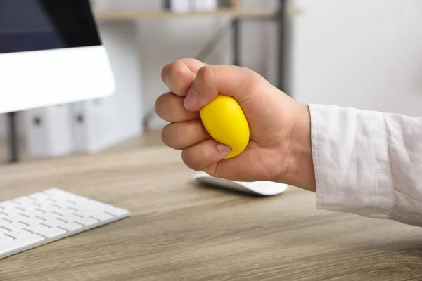 Man squeezing yellow stress ball in office, closeup