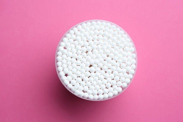 Many cotton buds in container on pink background, top view