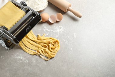 Pasta maker machine with dough and products on grey table, above view. Space for text