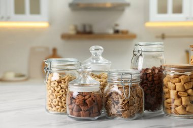 Glass containers with different breakfast cereals on white marble table in kitchen