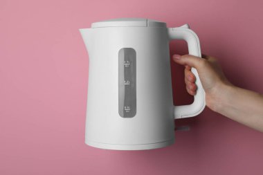 Woman holding modern electric kettle on pink background, closeup