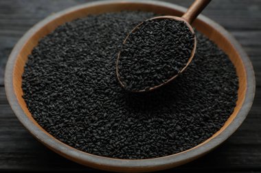Bowl and spoon with black sesame seeds on wooden table, closeup