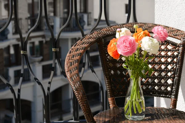 Bukiet Pięknych Jasnych Kwiatów Ranunculus Szklanym Wazonie Wiklinowym Fotelu Balkonie — Zdjęcie stockowe