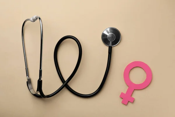 Female gender sign and stethoscope on beige background, flat lay. Women's health concept