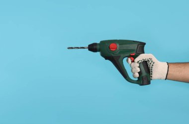 Açık mavi arka planda matkabı olan eldivenli işçi, yakın plan. Metin için boşluk