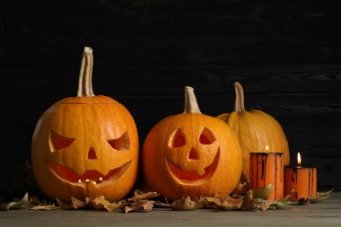 Korkunç yüzlü balkabakları ve siyah ahşap arka planda yanan mumlar. Geleneksel Cadılar Bayramı dekorasyonu